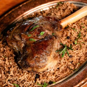 Juicy roasted lamb shank served on aromatic basmati rice garnished with herbs.